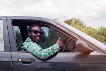 African man wearing sunglasses and smiling while sitting in a car with open front window.