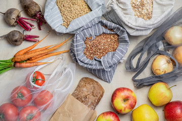 Groceries in reusable bags on natural flax or hemp background, top view. Concept of zero waste ethical shopping: food including fruit, vegetables, rice and cereal in bio packaging, flat lay view