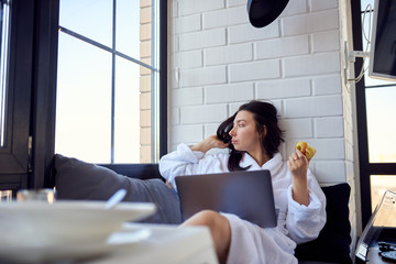 Girl in a bathrobe with a laptop eats an apple