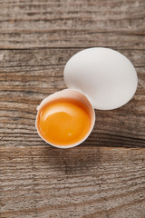 broken eggshell with yellow yolk near egg on wooden table