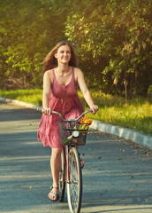 young woman in a dress rides a bike in a summer park.