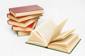 stack of books lies on a white wooden table, one book is opened, with text.