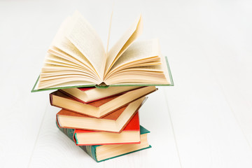 stack of books lies on a white wooden table, one book is opened, with text.