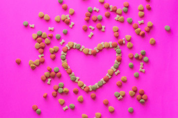 Creative valentines concept photo of Dog food and a heart be lovely on pink background.
