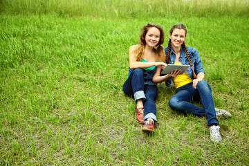 Fototapeta premium two friends with tablet computer sitting on the grass in the summer park. youth lifestyle.