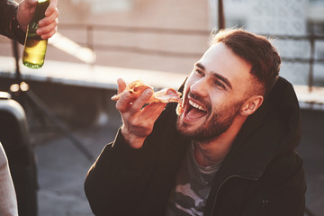 Guy eating a delicious pizza on the rooftop while having party with friends