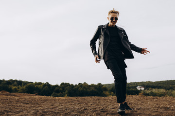 Young sexy man in leather jacket and sunglasses dancing outdoor. Silhouette against grey sky