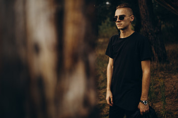 Young sexy man in black shirt and sunglasses standing outdoor in the forest