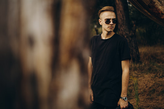 Young sexy man in black shirt and sunglasses standing outdoor in the forest
