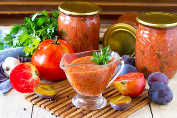 Homemade preserving. Tomato plum sauce with vegetables on the kitchen wooden background.