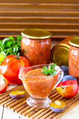 Homemade preserving. Tomato plum sauce with vegetables on the kitchen wooden background.