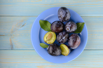 A plate of delicious ripe plum on the blue wooden table. Top view, copy space