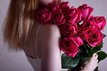 Young woman wearing a strap shoulderless dress is holding a big bouquet of pink roses