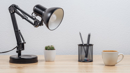 Workplace with a desk lamp, pencils, a cup of coffee and a pot with cactus. Light background.