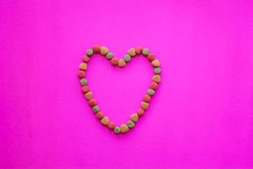 Creative valentines concept photo of Dog food and a heart be lovely on pink background.