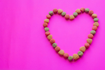 Creative valentines concept photo of Dog food and a heart be lovely on pink background.