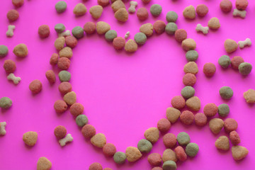 Obraz premium Creative valentines concept photo of Dog food and a heart be lovely on pink background.