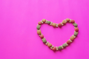 Obraz premium Creative valentines concept photo of Dog food and a heart be lovely on pink background.