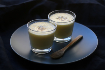 Two glasses of refreshing mango lassi drink, decorated with cardamom. Dark background, selective focus.