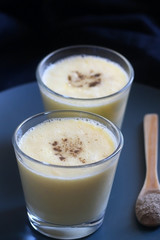 Two glasses of refreshing mango lassi drink, decorated with cardamom. Dark background, selective focus.