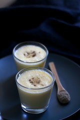 Two glasses of refreshing mango lassi drink, decorated with cardamom. Dark background, selective focus.
