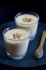 Two glasses of refreshing mango lassi drink, decorated with cardamom. Dark background, selective focus.