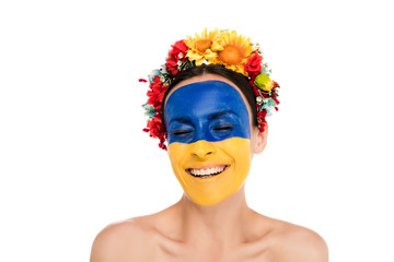 naked young woman in floral wreath with painted Ukrainian flag on skin smiling with closed eyes isolated on white