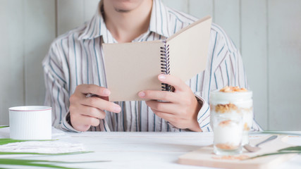 Select focus Asian male holding notebook with blur Healthy meal made of granola in glass foreground , thinking for recipes food