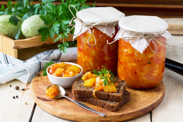 Homemade preserving. Baked Zucchini Salad with vegetables on the kitchen wooden background.