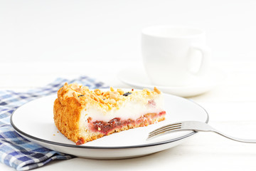 Piece of cake with cottage cheese souffle and plum decorated with almonds and blueberries on white wooden table