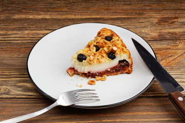 Piece of cake with cottage cheese souffle and plum decorated with almonds and blueberries on wooden table