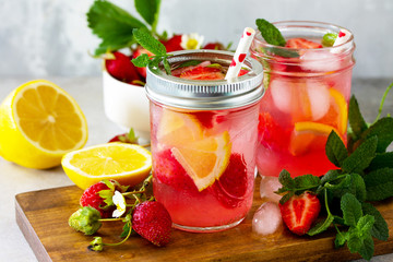 Fototapeta na wymiar Lemonade with fresh srtawberries, lemons and ice on a light stone or slate table.