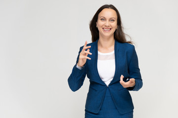 Portrait to the waist a young pretty brunette manager woman of 30 years in a business blue suit with beautiful dark hair. Standing on a white background, talking, showing hands, with emotions.