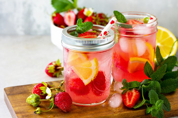 Lemonade with fresh srtawberries, lemons and ice on a light stone or slate table. Free space for your text.