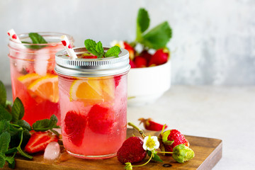 Lemonade with fresh srtawberries, lemons and ice on a light stone or slate table. Free space for your text.
