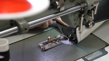 needle of the sewing machine quickly moves up and down. process of sewing leather goods. Tailor sews black leather in a sewing workshop. needle of the sewing machine in motion, close-up.