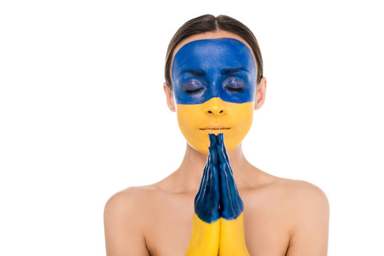naked young woman with painted Ukrainian flag on skin praying with closed eyes isolated on white