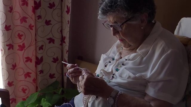elderly woman crocheting while sitting relaxed at home 