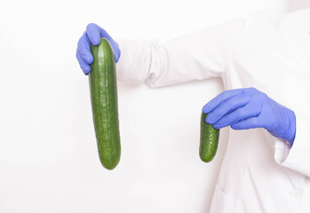 A doctor in medical gloves holds two different sized cucumbers. Concept of increasing penis in men,...