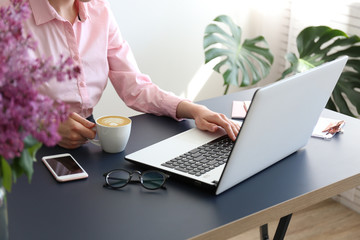Feminine freelance workspace concept. Woman's hands typing on white laptopp with black keyboard, desk with matte blue table top. Freelance blogger writing an article. Close up, copy space for text.