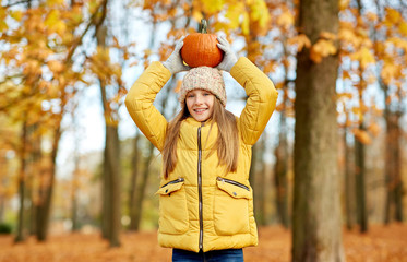 childhood, season and people concept - happy girl with pumpkin at autumn park