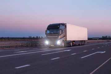 A black modern truck wagon transports cargo in a trailer refrigerator at night. Concept logistics and online stock exchange for the selection of goods and freight, copy space