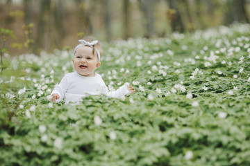 Little happy girl sits among the flowers in the woods