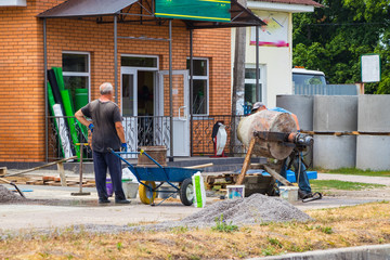 Builders are kneading a concrete solution with a concrete mixer.