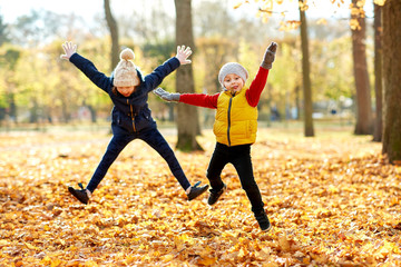 childhood, season and people concept - happy children running on fallen leaves at autumn park