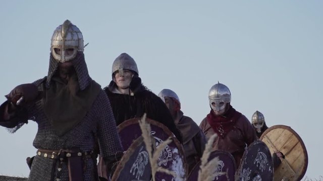 Group of medieval vikings with arms and shields going on the winter meadow.