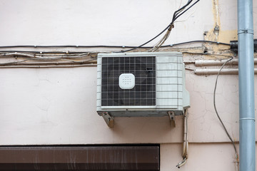 White air conditioning on the old wall of the house with the old wires of communication on the plastic drain pipe above the window. Cooling and comfort at home in the hot season.