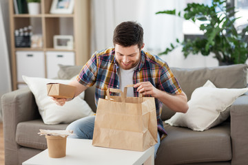 consumption, eating and people concept - smiling man unpacking takeaway food at home