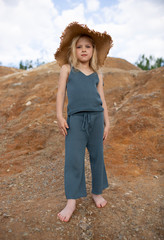 Little cute girl in stylish clothes on a background of rocks. Summer portrait of a little girl in a hat and cotton clothes for a magazine or advertisement