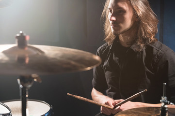 Portrait of a long-haired drummer with chopsticks in his hands sitting behind a drum set. Low key....